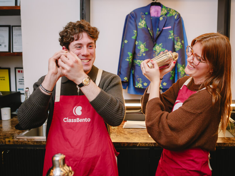 A smiling couple shaking cocktails together at a cocktail making class